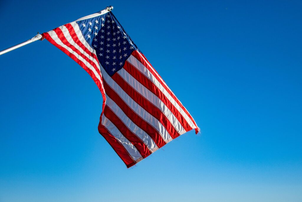 USA The American flag proudly waves on a flagpole against a clear blue sky, symbolizing freedom and patriotism.