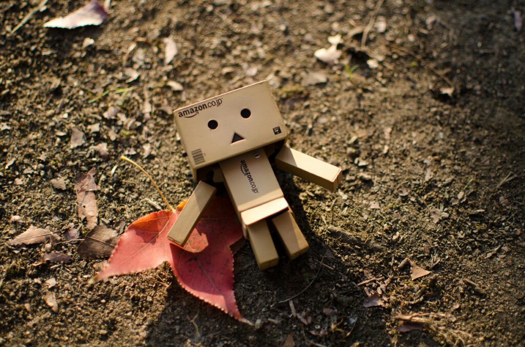 Cute cardboard robot toy on a dirt surface with autumn leaves, capturing a whimsical moment.