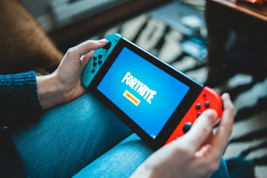 Close-up of hands holding a Nintendo Switch with Fortnite game screen indoors.
